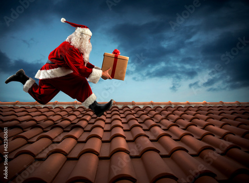 Santa Claus runs with a big present on a house roof photo