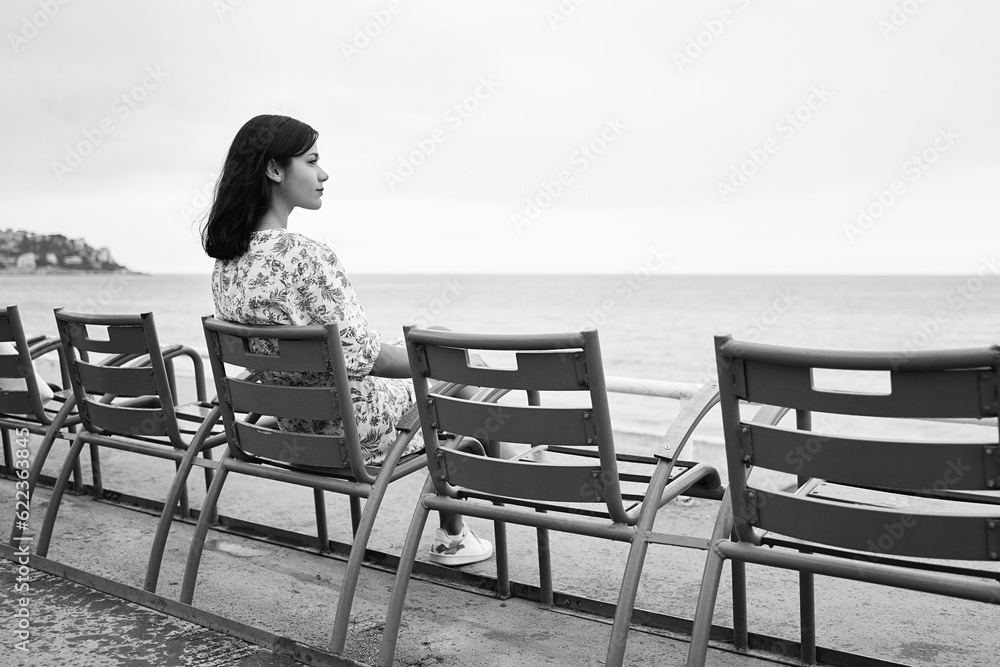 Beautiful smiling young mixed race woman sitting at one of the famous blue chairs at the Promenade des Anglais in Nice, France