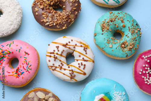 Different tasty glazed donuts on light blue background, flat lay
