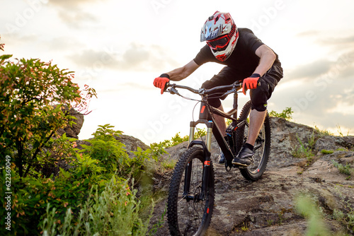 Professional Cyclist Riding the Bike Down Rocky Hill at Sunset. Extreme Sport Concept.