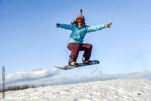 pretty young woman on the snowboard jumping over the slope in winter
