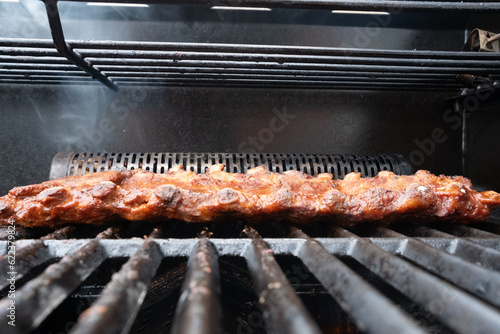 closeup of spareribs on a grill, with smoker and marinade