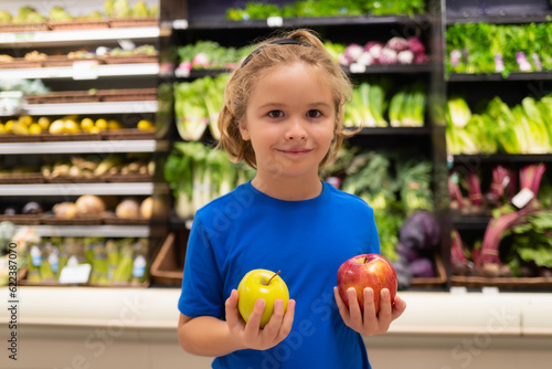 Kid with apple fruits at grocery store. Little child choosing food in grocery store or a supermarket.