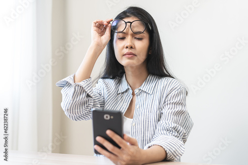 Presbyopia, Hyperopia middle aged asian woman holding eyeglasses problem with vision problem trying to read text, message from smart mobile phone screen, eye disease of old, eyesight farsightedness.