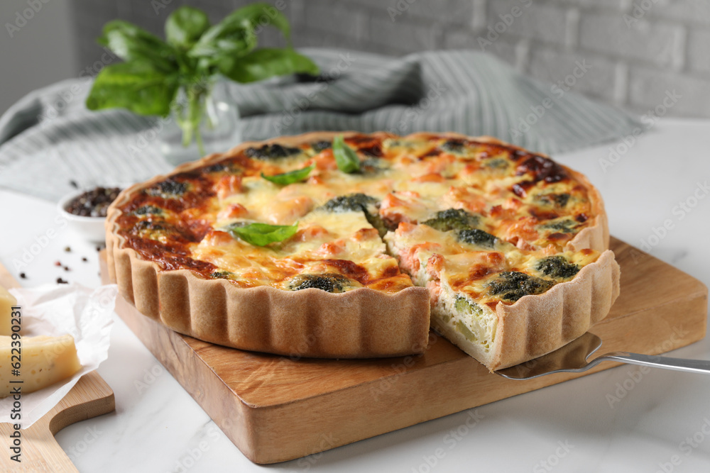 Taking piece of delicious homemade quiche with salmon and broccoli from wooden board on white table Taking piece of delicious homemade quiche with salmon and broccoli from wooden board on white table