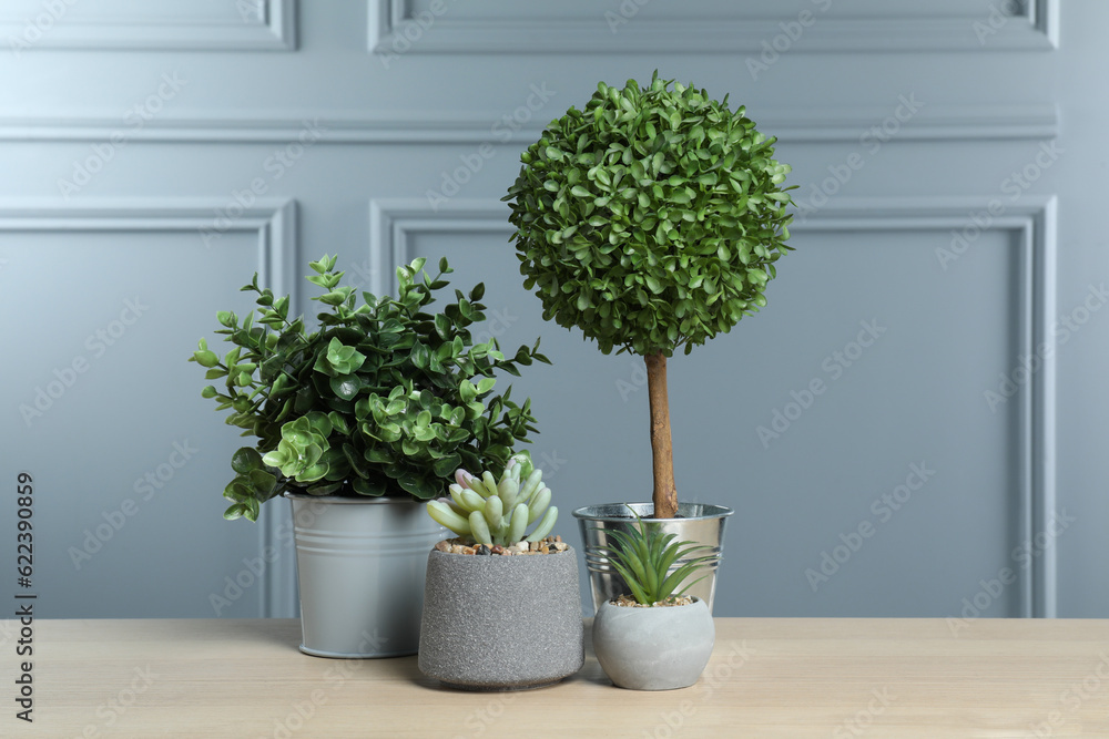 Many different artificial plants in flower pots on wooden table near grey wall Many different artificial plants in flower pots on wooden table near grey wall