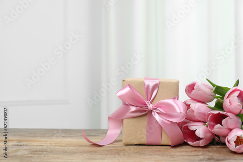 Beautiful gift box with bow and pink tulips on wooden table. Space for text