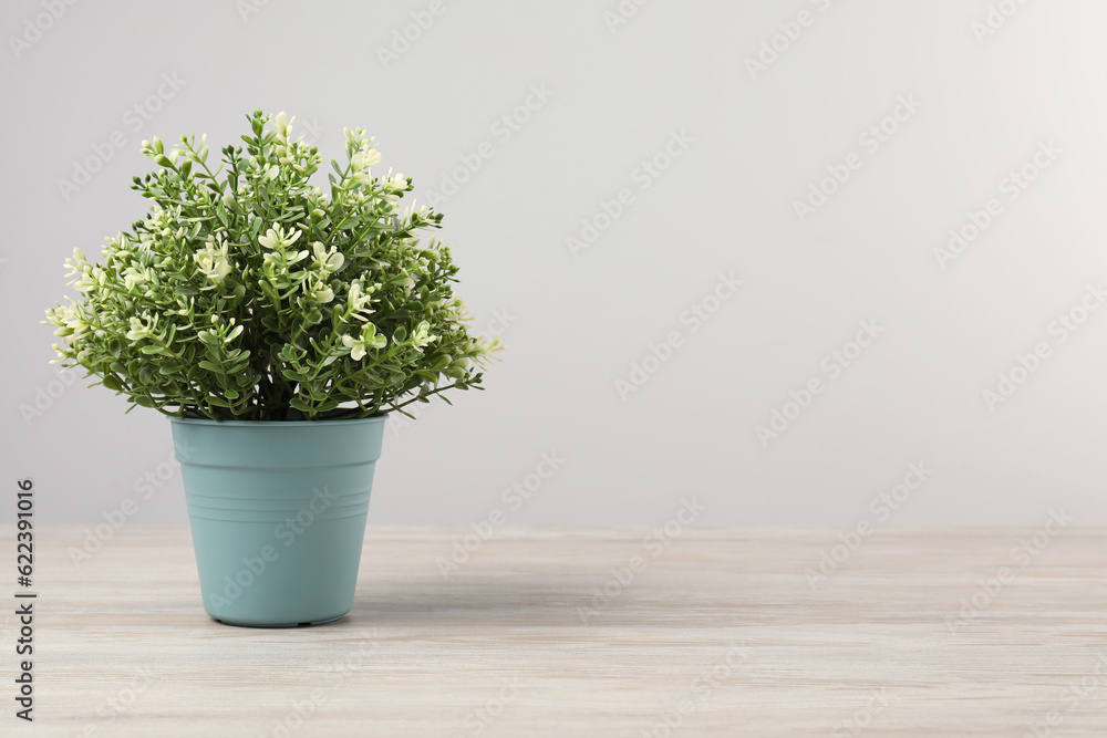 Beautiful artificial plant in flower pot on wooden table against light grey background, space for text Beautiful artificial plant in flower pot on wooden table against light grey background, space for text