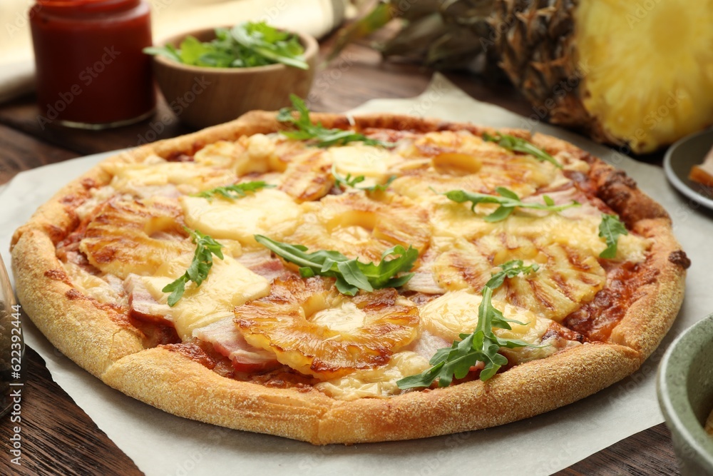 Delicious pineapple pizza with arugula on wooden table, closeup