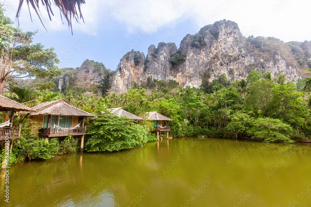 Fototapeta premium Charming wooden house on green lake with a stunning mountain view. Perfect retreat for those seeking a peaceful and natural escape. Concept of travel and rejuvenation.