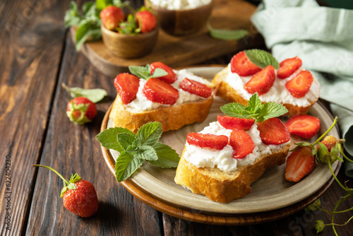 Berries toast breakfast, healthy food. Sandwich with strawberries and soft cheese on wooden background. Copy space.