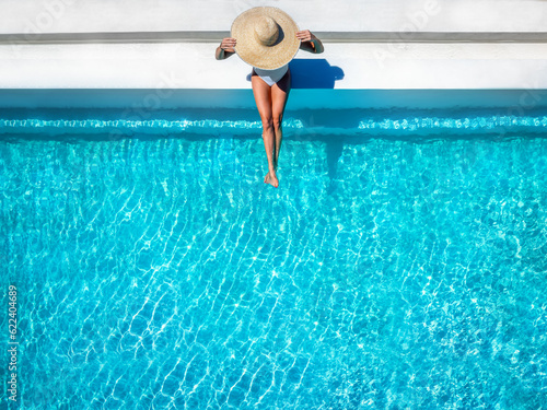 Aerial overhead view of a woman in a bathing suit and sunhat sitting on a pool edge with copy space, summer holiday travel concept