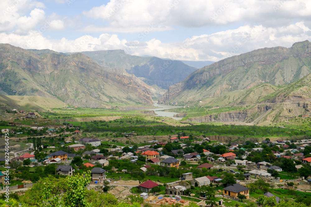 The landscape of the Caucasus Mountains and the village in the mountains on the background of a blue sky with clouds.