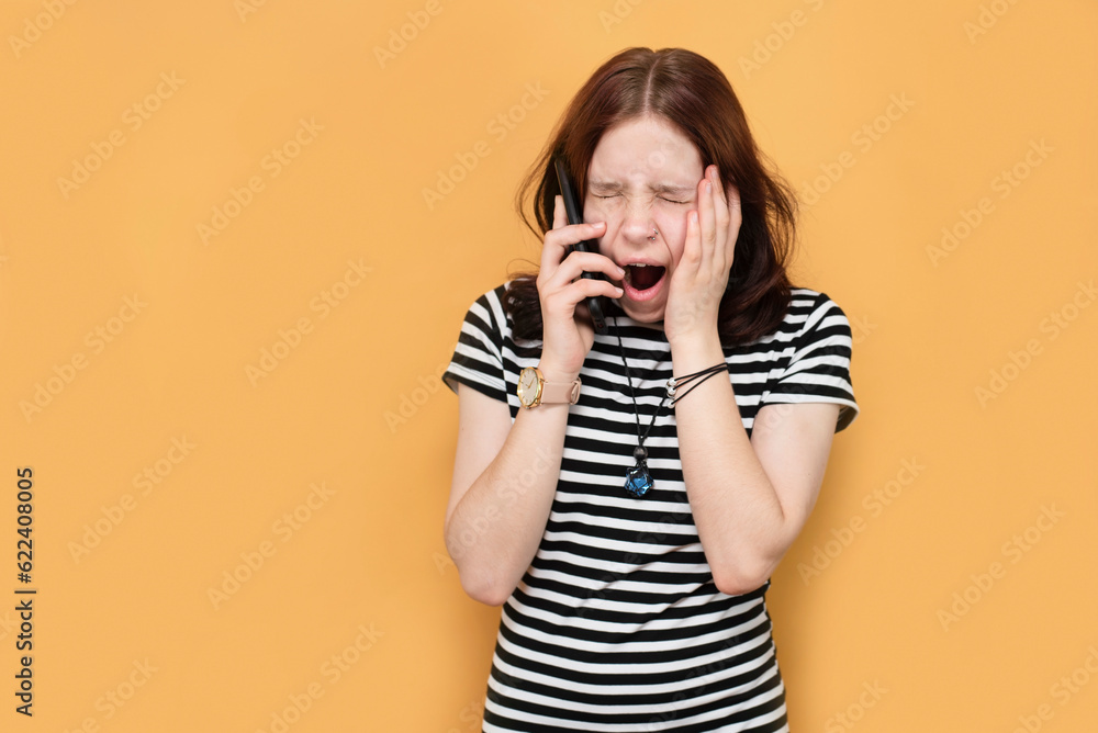 A young teenage girl is very tired from studying and yawns, calls her English tutor that she cannot come to class today. A tired girl yawns on a yellow background A young teenage girl is very tired from studying and yawns, calls her English tutor that she cannot come to class today. A tired girl yawns on a yellow background