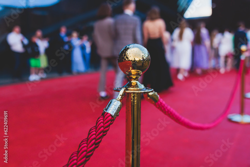 Red carpet with ropes and golden barriers on a luxury party entrance, cinema premiere film festival event award gala ceremony, wealthy rich guests arriving, outdoor decoration elements, summer day