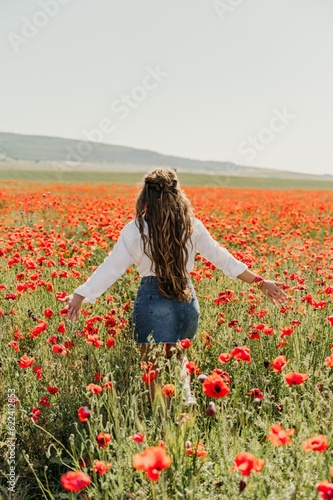 Woman poppies field. Back view of a happy woman with long hair in a poppy field and enjoying the beauty of nature in a warm summer day.