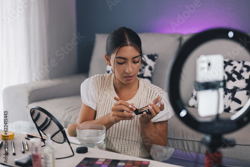 Focused female blogger shooting beauty video while doing makeup photo