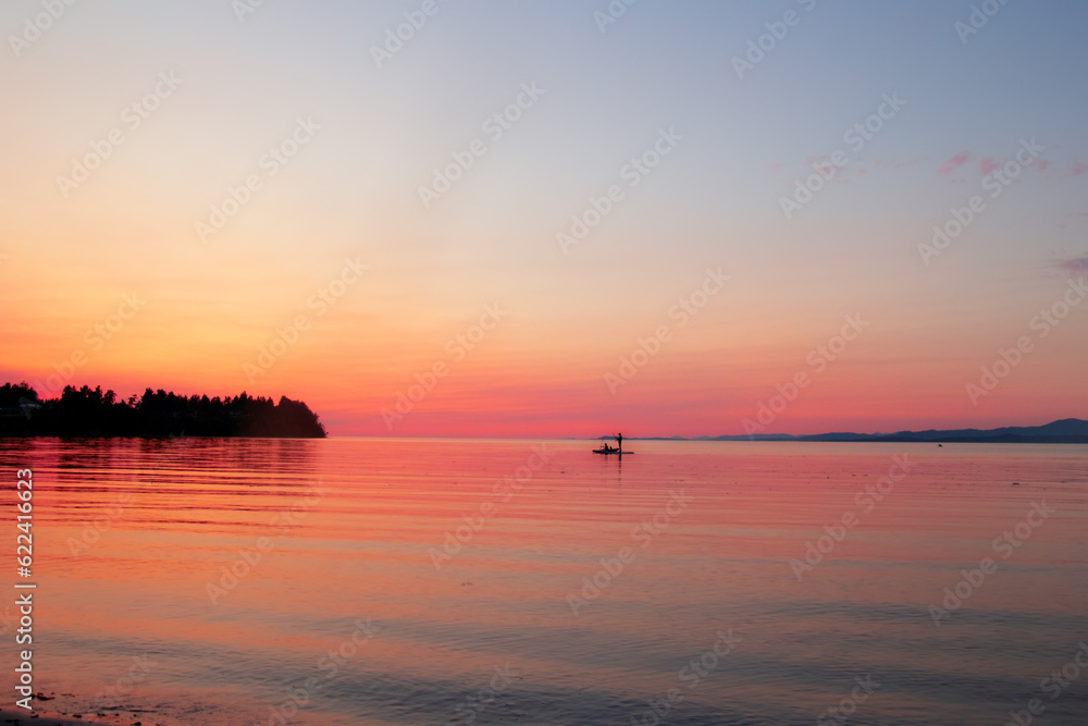 Ocean beach in sunrise and silhouette of a man on paddle boat.