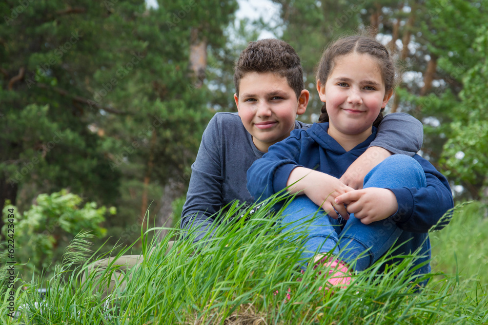 In summer, a brother and sister sit on the grass in the forest. In summer, a brother and sister sit on the grass in the forest.