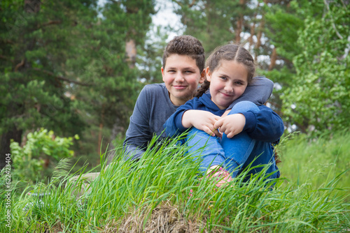 In summer, a brother and sister sit on the grass in the forest. © Олеся Тамилович