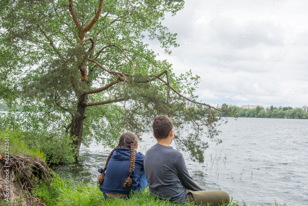 Fototapeta premium In summer, a brother and sister sit on the river bank.