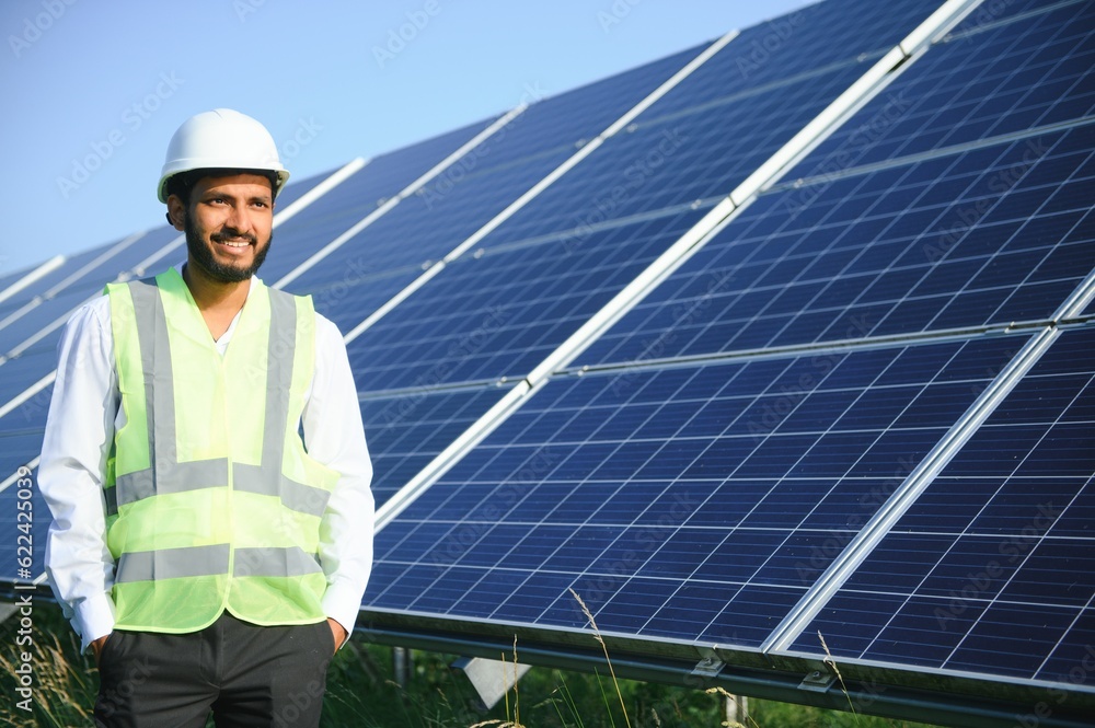 An Indian male engineer in a green vest is working on a field of solar panels. The concept of renewable energy. An Indian male engineer in a green vest is working on a field of solar panels. The concept of renewable energy.
