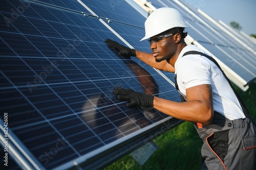 African American engineer maintaining solar cell panels. Technician working outdoor on ecological solar farm construction. Renewable clean energy technology concept