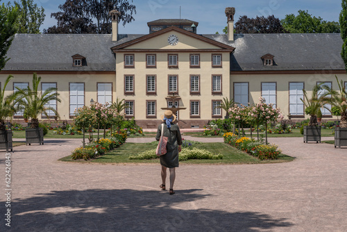 Strasbourg, France - 06 26 2023: Orangerie Park: A woman wearing a straw hat with a blue ribbon walking toward The Josephine pavilion. © Franck Legros
