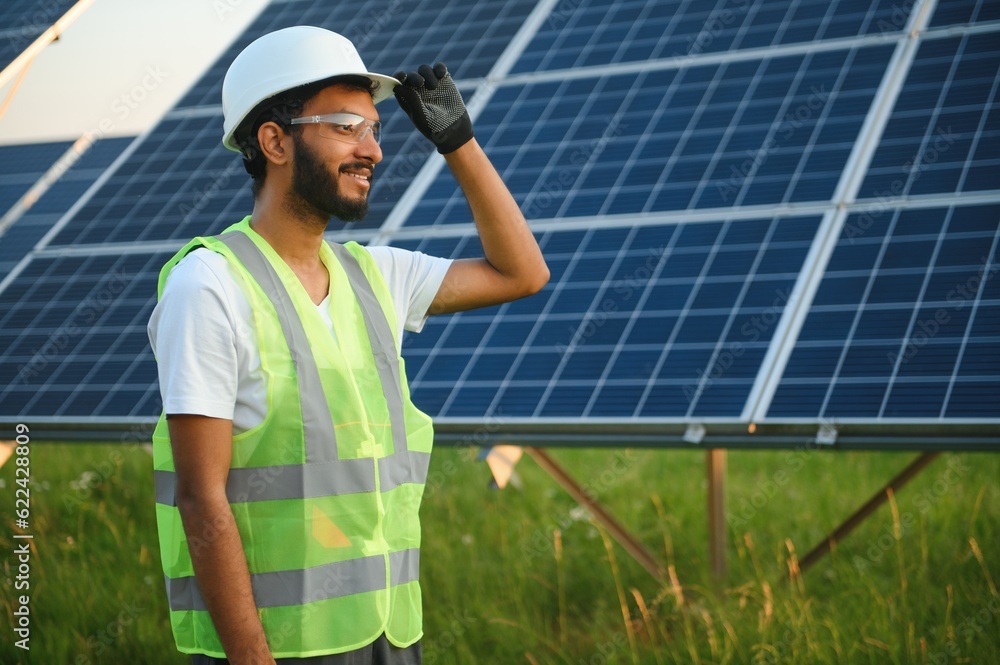 An Indian male engineer in a green vest is working on a field of solar panels. The concept of renewable energy. An Indian male engineer in a green vest is working on a field of solar panels. The concept of renewable energy.