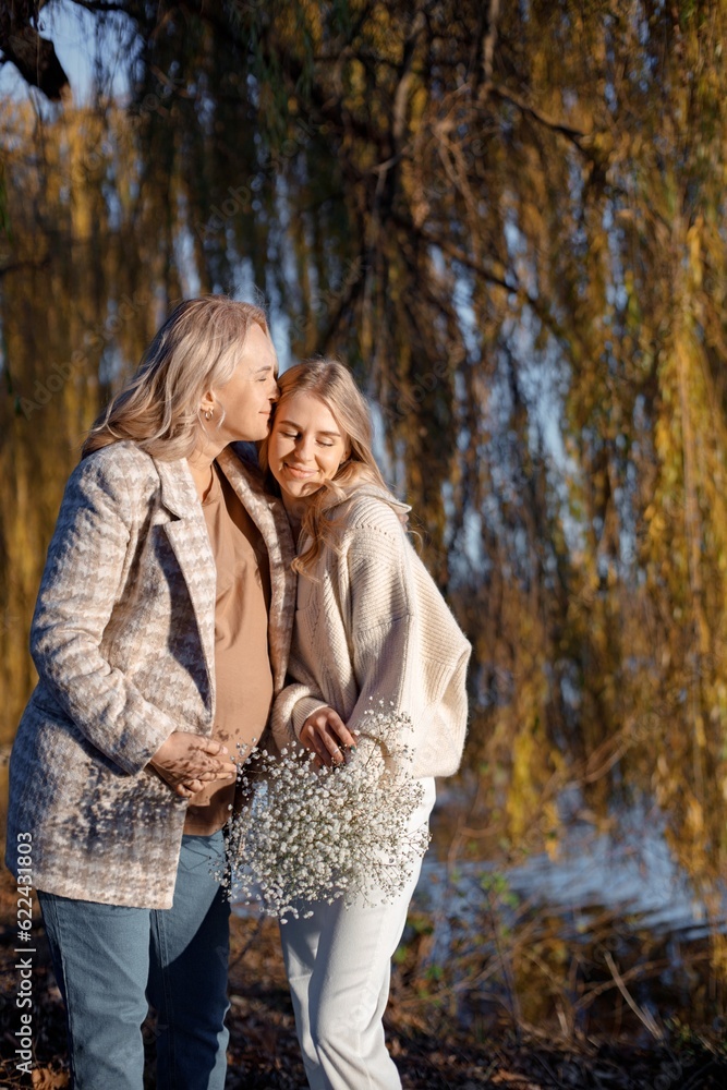 Fototapeta premium Adult daughter hugs her pregnant mom while standing in autumn park