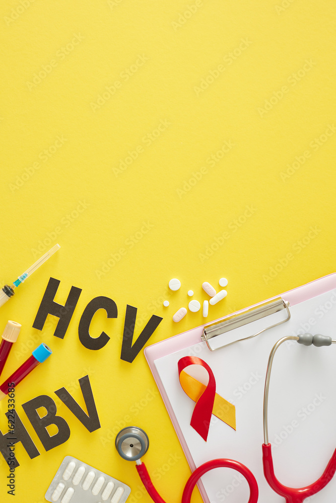 Fototapeta premium World Hepatitis Day. Top view vertical shot of liver, pills, stethoscope, clipboard, HBV, HCV abbreviation, awareness ribbon, blood samples and syringe on yellow background with space for text