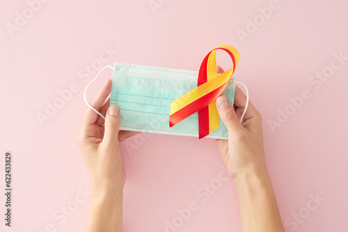 Healthcare on International Hepatitis Day. First person top view photo of medical mask, awareness ribbon on light pink background