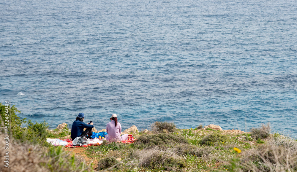 Fototapeta premium Young couple doing picnic by the sea. People relaxing outdoors