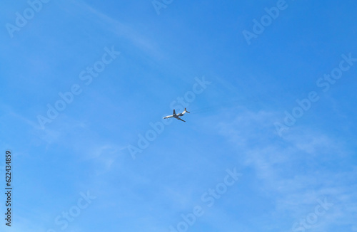 The plane flies high in the blue sky with small clouds