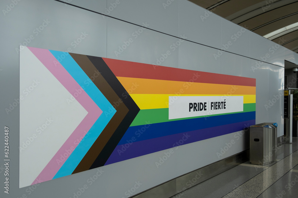 LGBTQ+ rainbow flag on the wall with sign Pride in English and French ...