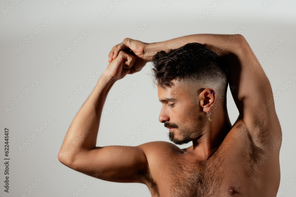 A healthy, athletic young man poses with one arm bent over his head and his other arm holding a bicep flex. He looks athletic, fit, and muscular. A healthy, athletic young man poses with one arm bent over his head and his other arm holding a bicep flex. He looks athletic, fit, and muscular.