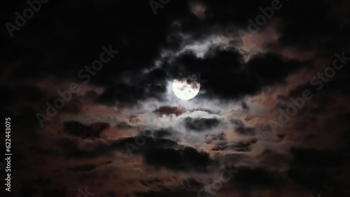 Full moon on a dark cloudy night with clouds flying in front of the moon like in thrillers and horror movies. Dark night sky, black clouds. Real shooting