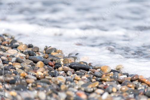 Colored pebbles on the beach of Greece with the waves of the sea covering them during a sunny day.