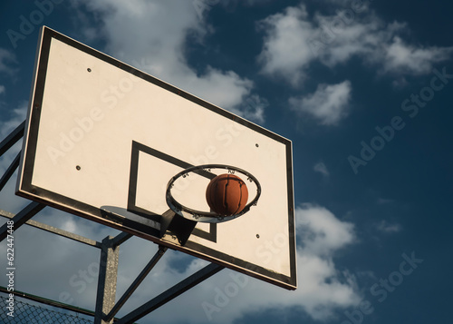 Piłka do koszykówki wpadająca do kosza, na tle błękitnego, słonecznego nieba.