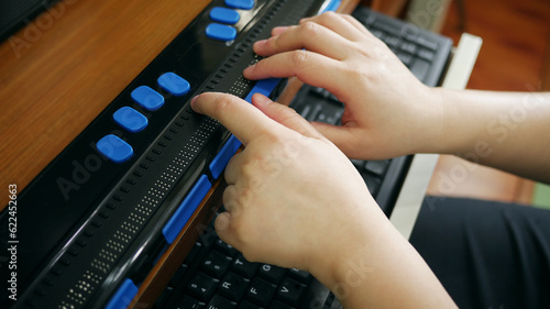 Photos Close-up hands of person with blindness disability using computer with braille d