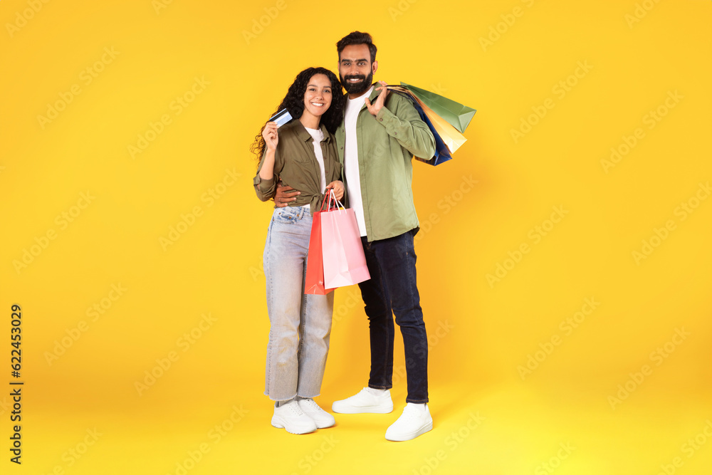 Arabic Couple With Shopper Bags Showing Credit Card, Yellow Background Arabic Couple With Shopper Bags Showing Credit Card, Yellow Background