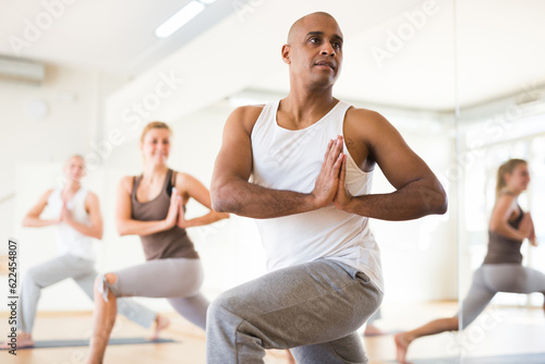 Hispanic man practicing Parvritta Parsvakonasana (reversed side angle pose) during group yoga training