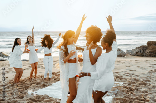 Group of happy young ladies dancing at the beach on beautiful summer sunset, celebrating bachelorette party photo