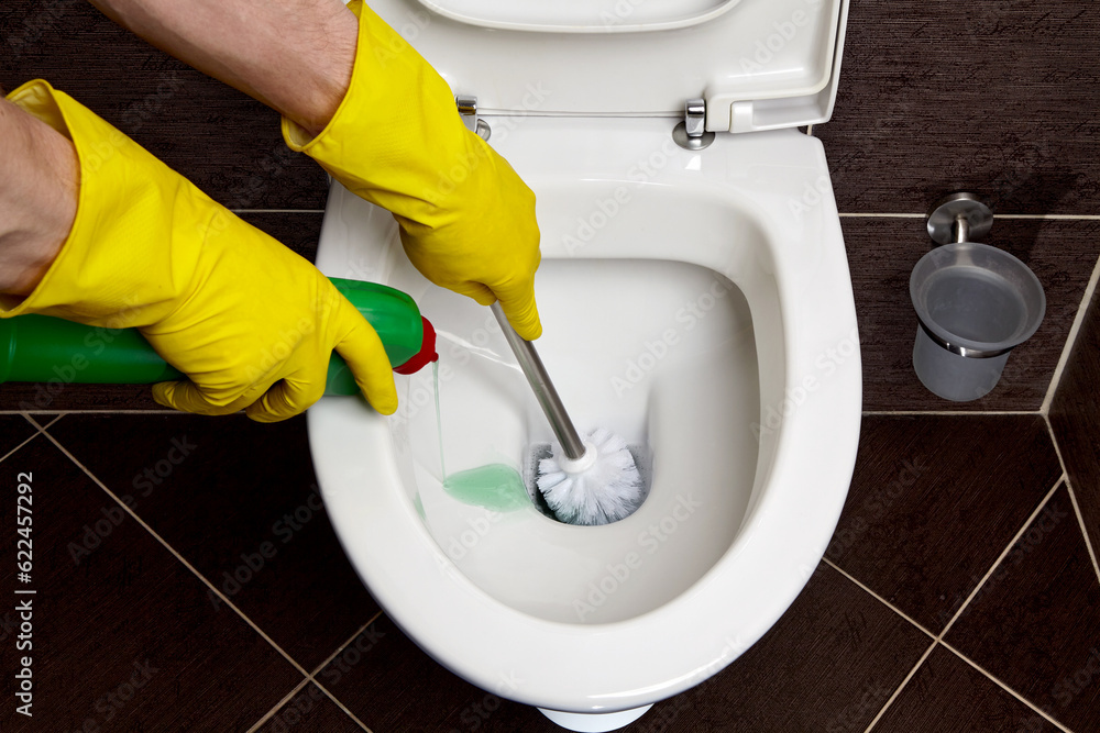 a person in yellow rubber gloves washes and disinfects toilet bowl with brush and disinfectant solution a person in yellow rubber gloves washes and disinfects toilet bowl with brush and disinfectant solution