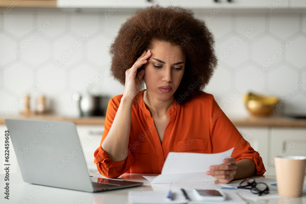 Stressed Black Female Entrepreneur Reading Papers And Working On Laptop At Home Stressed Black Female Entrepreneur Reading Papers And Working On Laptop At Home
