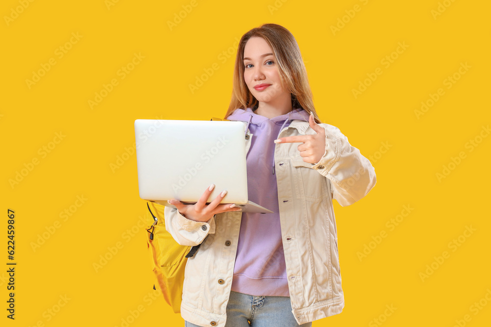 Female student pointing at laptop on yellow background Female student pointing at laptop on yellow background