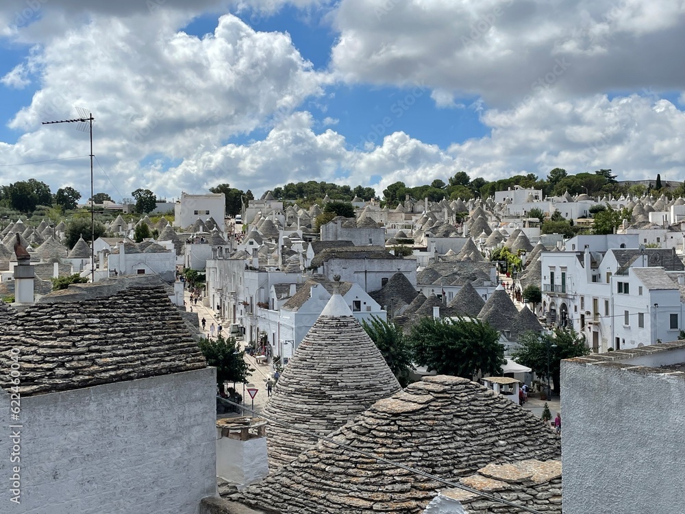 panorama of old rural houses with roofs of gray brown stone against the blue sky and white clouds on a summer day Italy proud of Alberobello