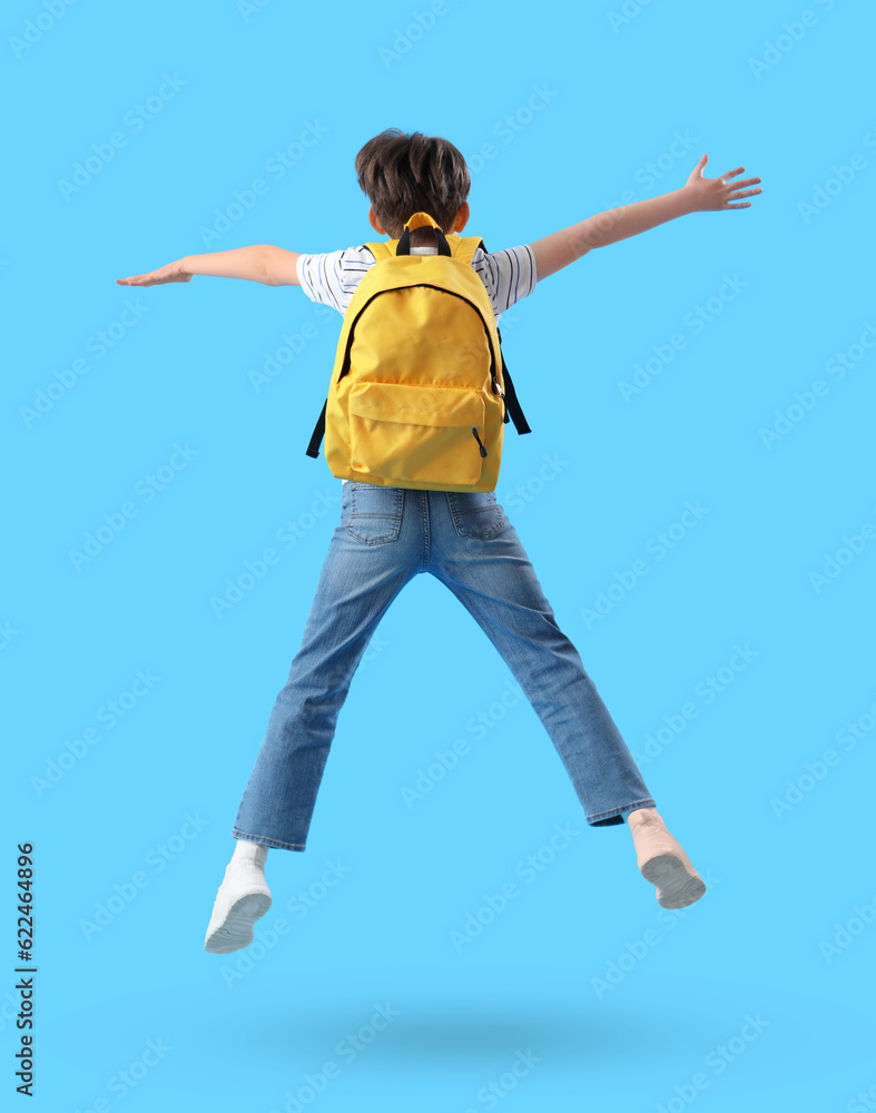 Jumping little boy with schoolbag on blue background, back view Jumping little boy with schoolbag on blue background, back view