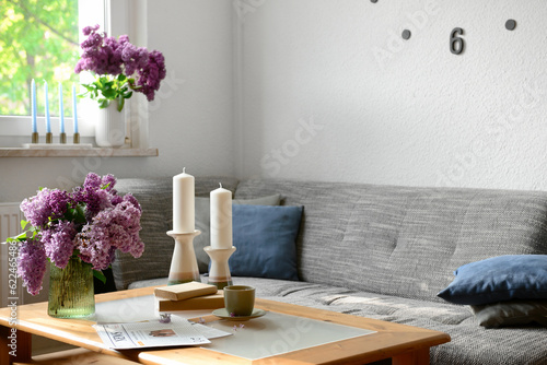Interior of light living room with beautiful lilac flowers, candles, table and sofa © Pixel-Shot