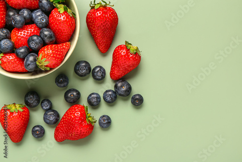 Foto Bowl with fresh blueberries and strawberries on green background